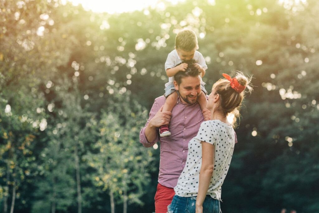 father holding toddler over shoulders smiling at mother
